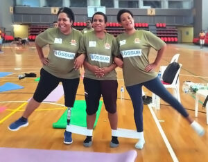 Three women standing in line, exercising using two rubber bands between legs.